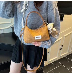 Close-up of brown suede handbag featuring a white modish label and a cute bear plush toy