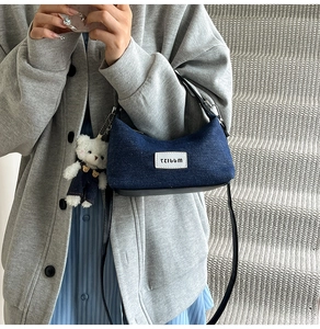 Detail of blue denim crescent bag with a white bear plush charm on grey background