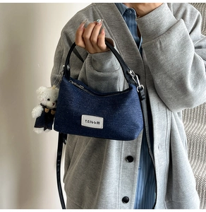 Detail of denim hobo bag with black leather handle and cute white teddy bear charm