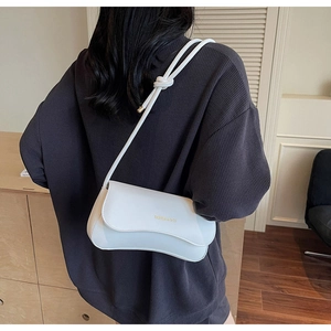 Detail of creamy white geometric crossbody bag with knot strap and gold lettering logo