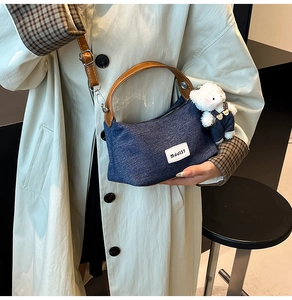 Detail of blue denim dumpling bag featuring leather handles and a cute plush bear charm
