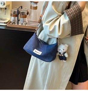 Détail du sac bandoulière en denim avec bandoulière en cuir brun et breloque ours en peluche