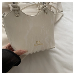 Detail of a beige handbag featuring marble texture and a knotted pleated handle design