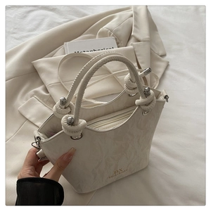 Detail of cream handbag showing crinkled leather texture and knotted handle with metal accents