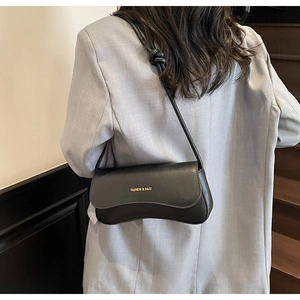 Detail of a crescent-shaped black leather shoulder bag featuring gold branding and knot straps