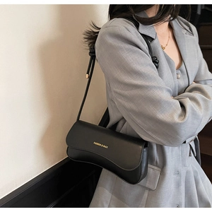 Détail d'un sac sous le bras noir rétro avec lettrage doré sur un modèle en costume