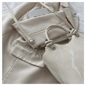 Detail of a creamy white glossy patent leather handbag with a geometric rope handle