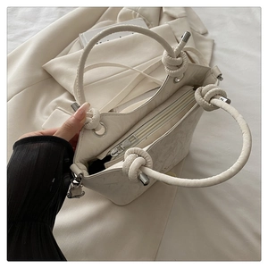 Close-up of knotted handle detail and silver hardware on cream leather handbag