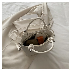 Detail view of woven knotted handle and spacious inner compartment of cream handbag