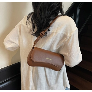 Detail of brown leather underarm bag with wavy flap design and knot strap on shoulder