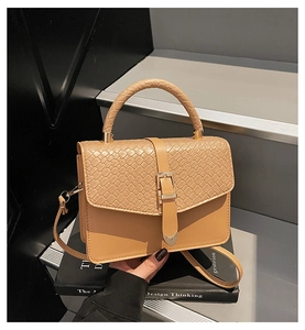 Détail du sac beige avec rabat en cuir tressé et boucle métallique sur des marches