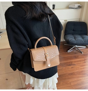 Détail d'un sac porté épaule marron à rabat tressé et fermoir cœur en métal