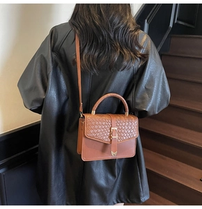 Détail de sac marron avec motif tressé, pendentif cœur doré et bandoulière élégante