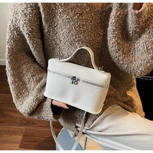 Detail of white lychee texture handbag with silver zipper and slim strap over brown sweater