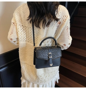 Détail d'un sac à bandoulière en cuir noir avec rabat texturé porté par un mannequin
