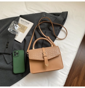 Détail d'un sac à main kaki avec rabat tissé et boucle métallique sur un blazer gris