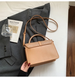 Gros plan d'un sac à main kaki avec détails tissés posé sur un blazer gris chic