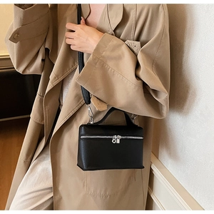 Vista laterale della borsa vanity in pelle nera con cerniera argento su un trench coat
