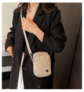 Detail of khaki nylon crossbody bag with LYT logo worn over a black blazer