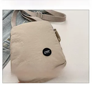 Detail view of a beige nylon crossbody bag featuring a circular LYT letter patch decoration