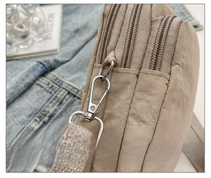 Detail of khaki nylon crossbody bag showing three-layer zippers and silver metal hardware