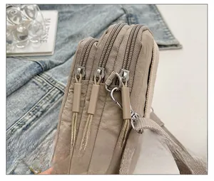 Detail view of khaki nylon crossbody bag featuring three smooth metal zipper compartments