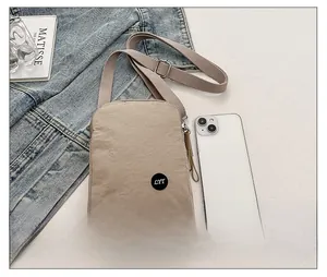 Macro view of compact light khaki nylon crossbody bag shown next to a smartphone