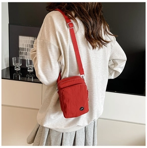 Detail of red nylon crossbody bag with multi-zipper layers and adjustable shoulder strap