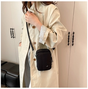Detail of compact black nylon crossbody phone bag with adjustable strap on model