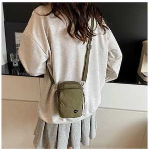 Close-up of olive green nylon crossbody bag with dual zippers and adjustable strap