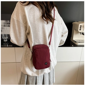 Close-up of wine red nylon crossbody bag with dual zippers and logo detail on strap