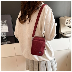 Rear view of a model wearing the wine red mini nylon crossbody bag with adjustable strap
