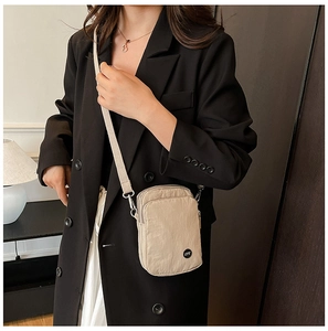 Detail of beige nylon crossbody bag featuring multiple zippers and adjustable woven strap