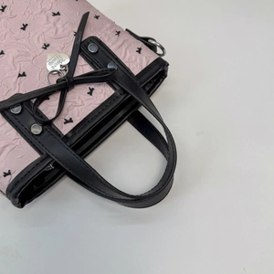 Détail d'un sac à main plissé rose avec des imprimés de chiens et un pendentif cœur