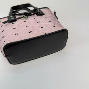 Détail du sac à main rose plissé avec imprimés nœuds noirs et breloque cœur