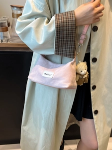 Pink suede underarm bag with cute teddy bear charm shown on a beige trench coat
