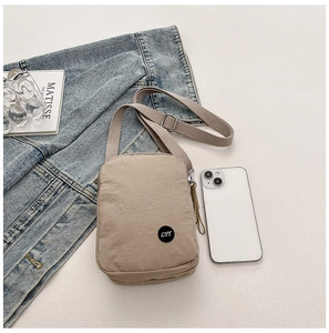 Detail view of a beige nylon crossbody bag featuring adjustable straps and a small logo