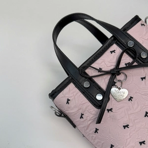 Détail d'un sac plissé rose avec motifs de chats, nœud noir et pendentif cœur en métal