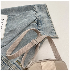 Detail of beige crossbody bag featuring adjustable nylon strap and silver metal hardware