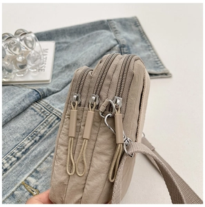 Detailed side view of beige nylon crossbody bag with three zipper compartments and woven strap