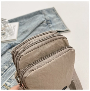 Close-up of khaki nylon crossbody bag showing three zipper compartments and fabric strap