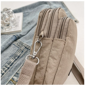 Detail of khaki nylon crossbody bag showing triple zipper compartments and silver hardware