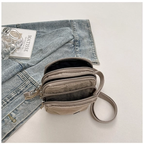 Detailed top view of a khaki nylon crossbody bag with triple zipper layers and strap