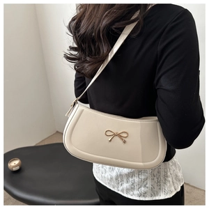 Close-up of cream glossy shoulder bag with golden bow hardware and sleek crescent design