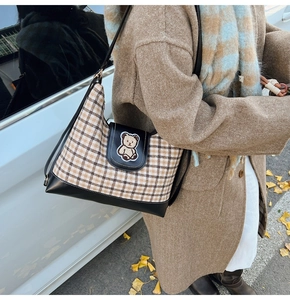 Detail of checkered canvas tote bag with embroidered bear patch on leather flap
