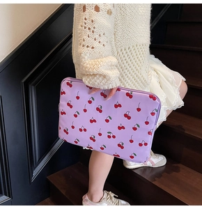 Chic lavender laptop sleeve with red cherry prints shown held by a model on stairs