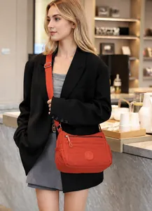 Detailed view of an orange-red nylon crossbody bag worn by a model in a casual setting