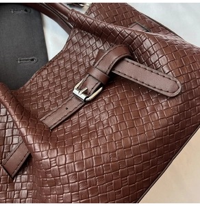 Detailed macro view of dark brown woven texture and silver buckle on the leather handbag