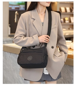 Detail of a black nylon crossbody bag with adjustable wide strap and round logo patch