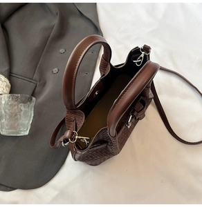 Close-up of woven dark brown leather texture with metallic magnetic buckle on a bucket bag